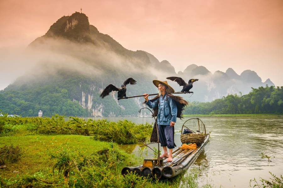 Señor pescador en un lago en las montañas de Yangshuo Cormoran en china